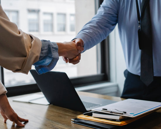 Two people shaking hands over a desk in an office